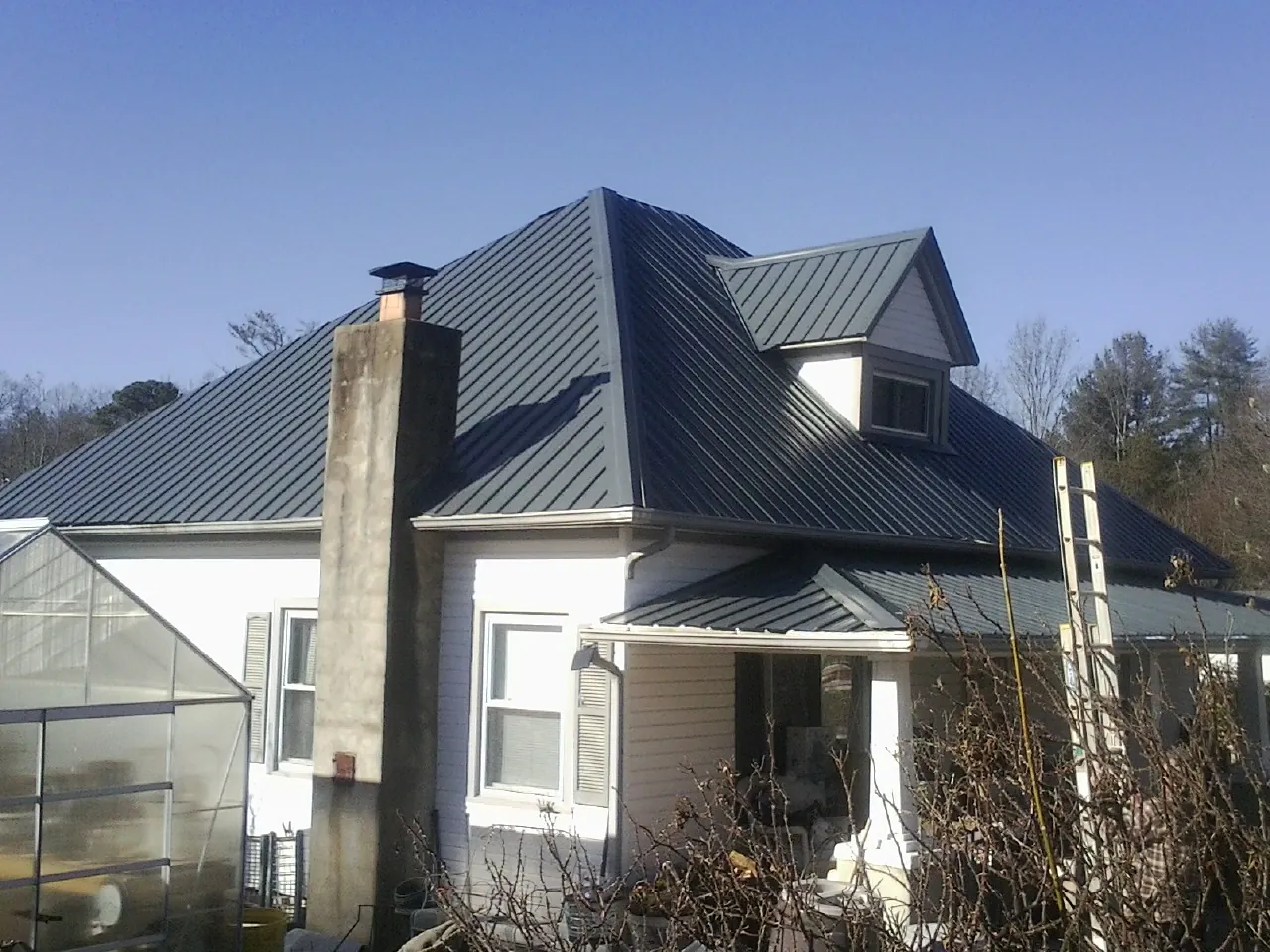 Dark blue standing seam metal roof on a white farmhouse with dormer — Slate & Tile Roof Repair by Roofing Brothers in Valley Grove