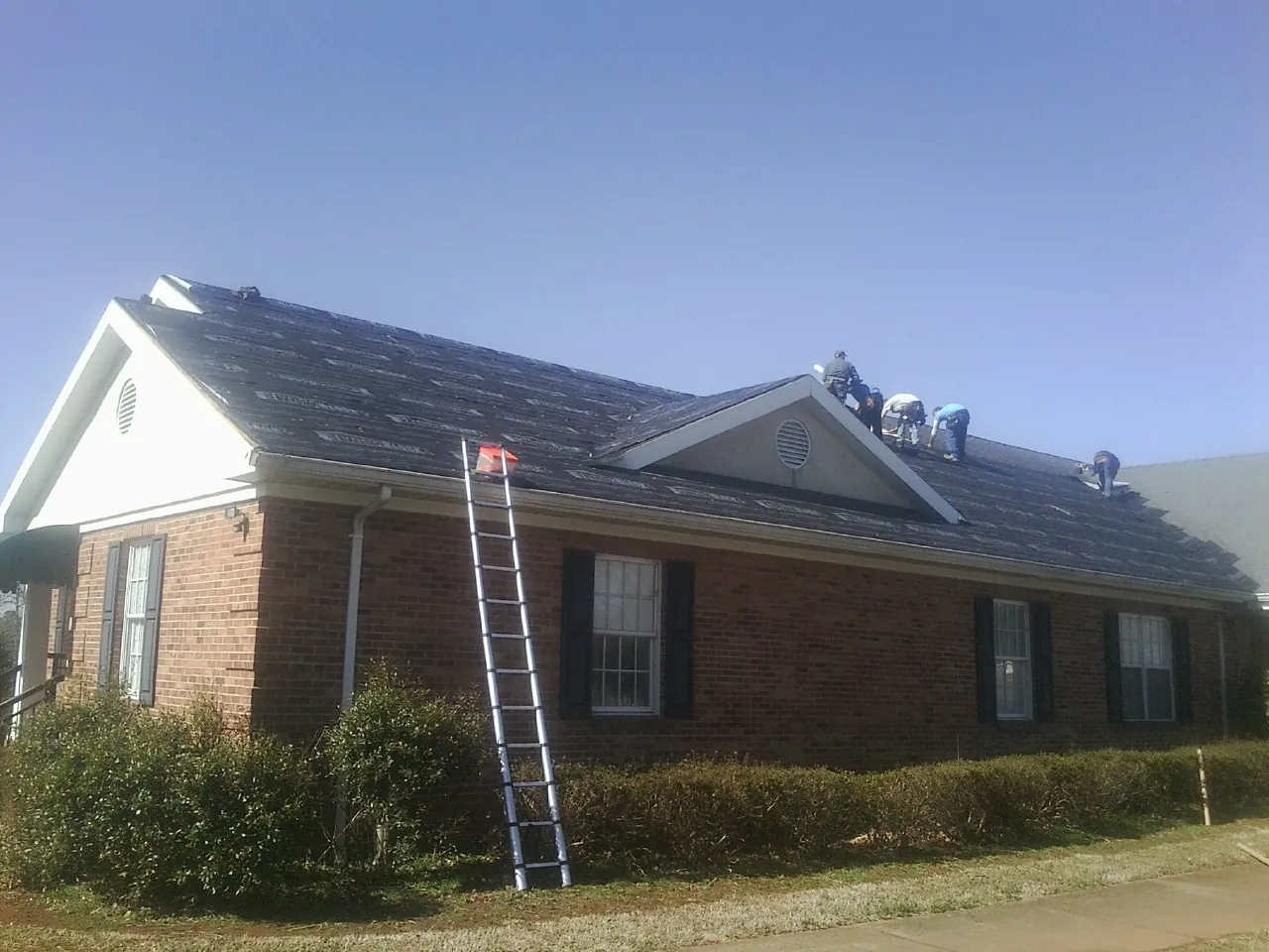 Crew tearing shingles off a brick ranch roof with a ladder set — Emergency Roof Repair work by our crew in Valley Grove