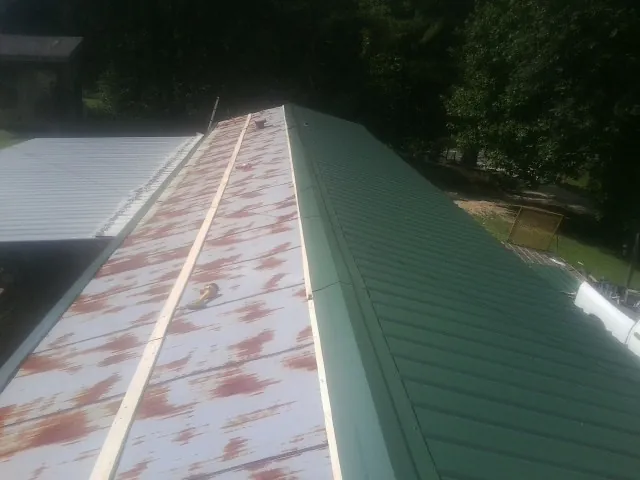 Old rusted panels beside newly installed green metal roofing — Wind Damage Roof Repair by Roofing Brothers in Valley Grove