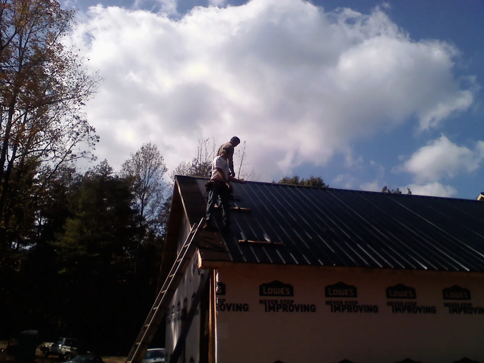 Roofer fastening dark metal panels high against a cloudy sky, from a Roof Inspection job in Valley Grove