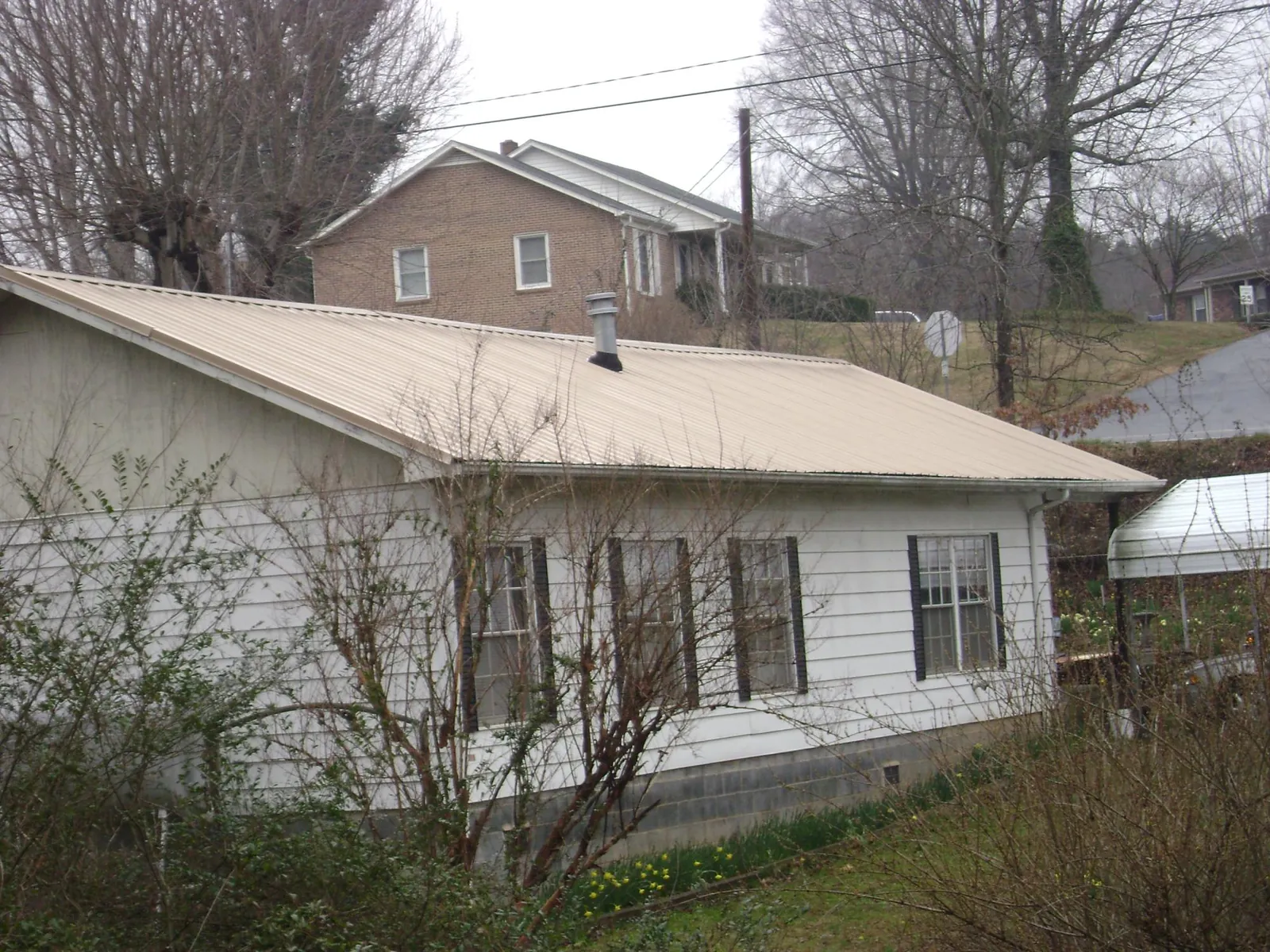Tan metal roof on a white sided house set into a hillside — Commercial Roofing by Roofing Brothers in Valley Grove
